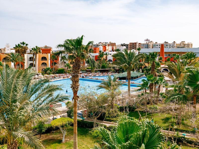 Großer Hotelpool mit Palmen und mehrstöckigen Gebäuden im Hintergrund bei klarem Himmel.