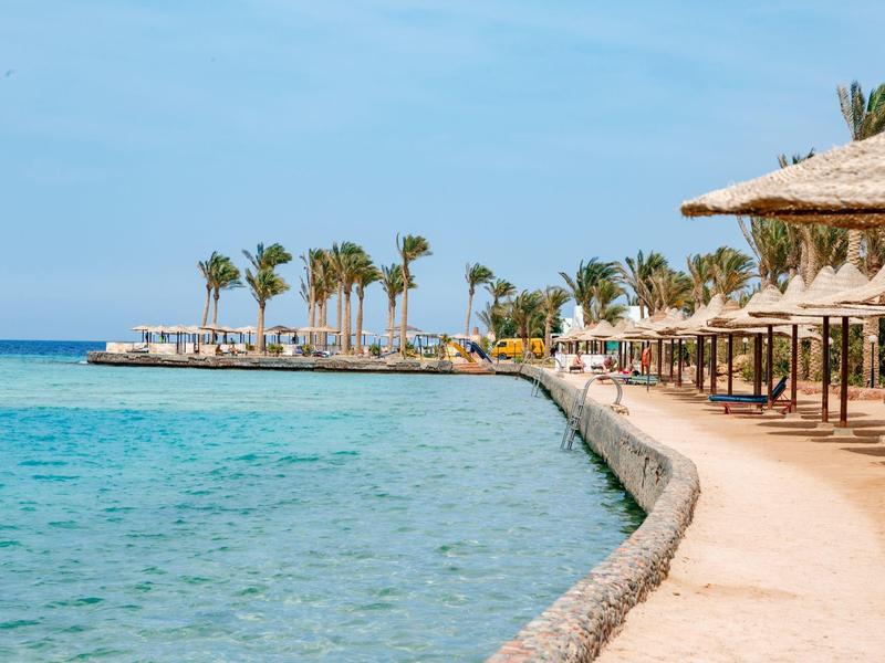 Promenade am Meer mit Palmen und Sonnenschirmen an einem sonnigen Urlaubsort.