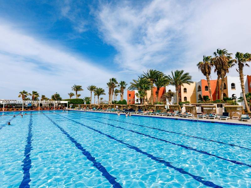 Großer Außenpool mit klar blauem Wasser und Palmen unter blauem Himmel.