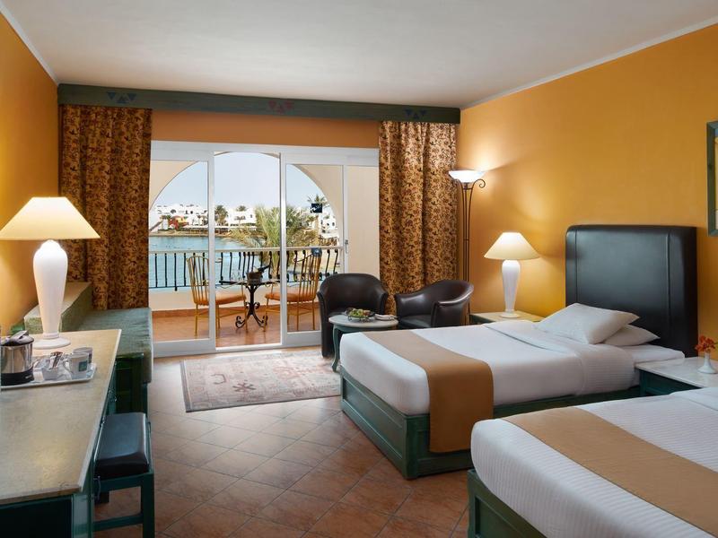 Hotelzimmer mit zwei Betten, Schreibtisch, Fernseher und Balkon mit Meerblick.