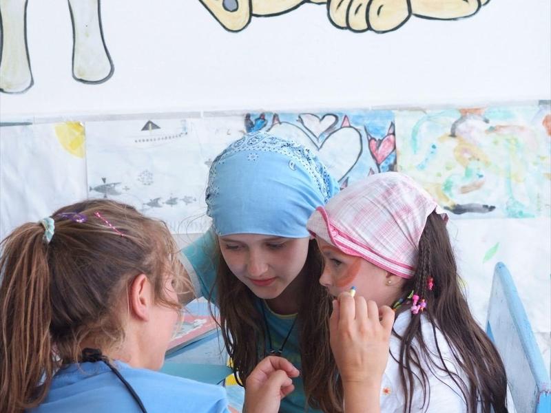 Drei Mädchen sitzen zusammen, eines malt auf das Gesicht eines anderen.