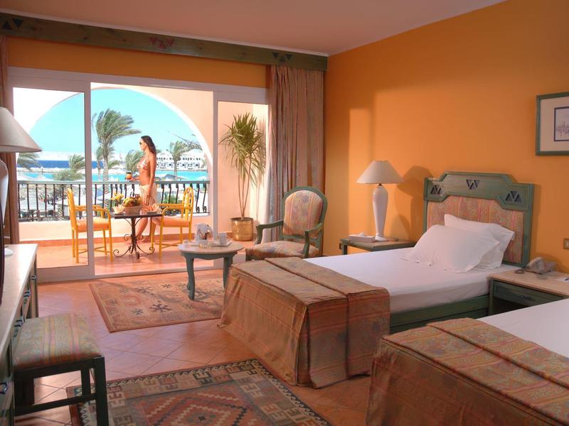 Hell eingerichtetes Hotelzimmer mit Balkon, Blick aufs Meer und möbliertem Außenbereich.