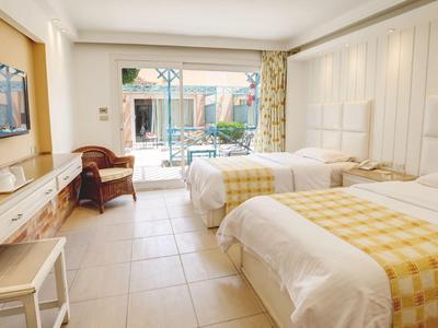 Helles Hotelzimmer mit zwei Betten, gelb karierten Decken, Flachbildschirm und Zugang zur Terrasse.