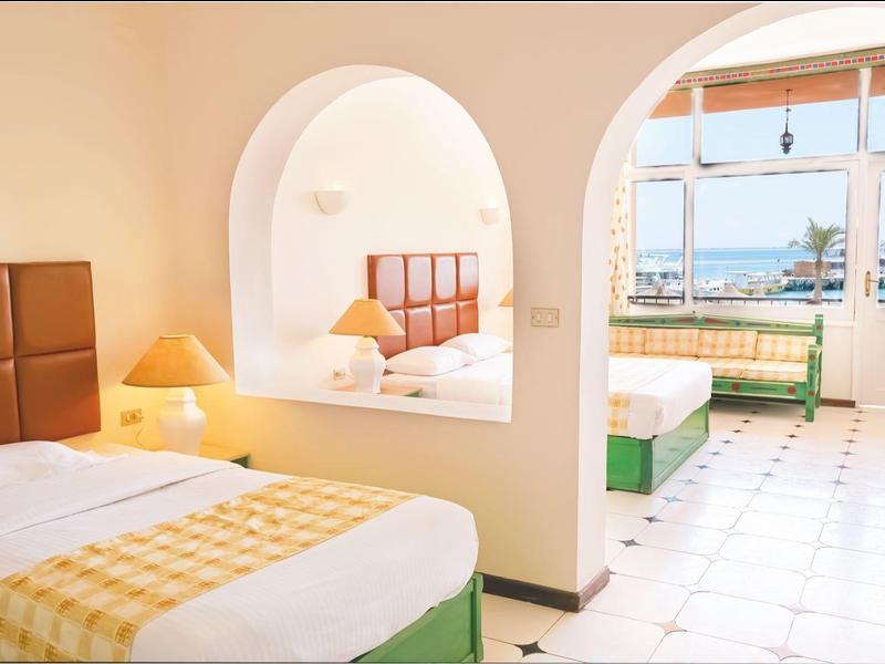 Helles Hotelzimmer mit zwei Bereichen, Betten, gelben Kissen und Blick aufs Meer.