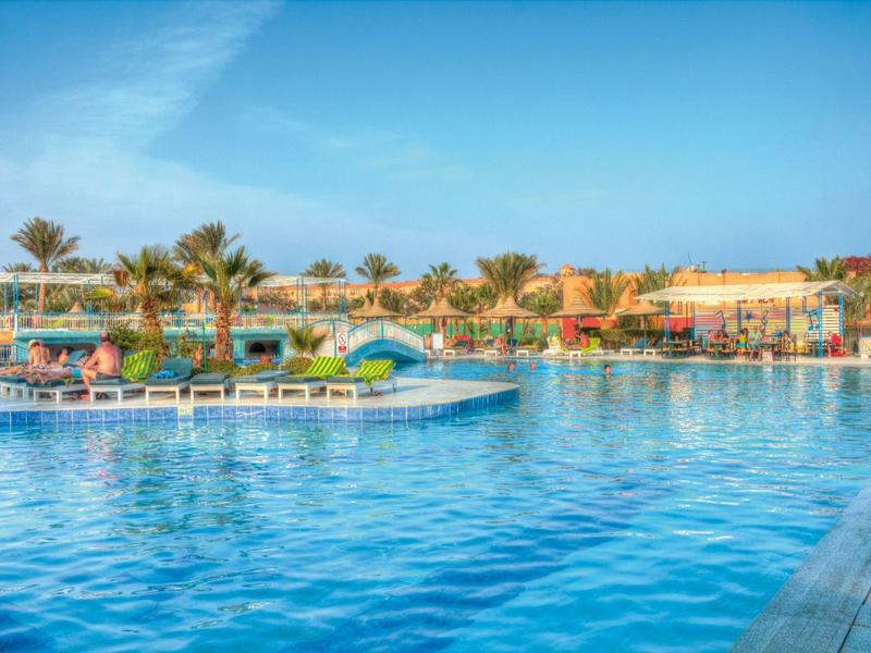 Großer Resort-Pool mit Liegestühlen und Palmen unter klarem Himmel.