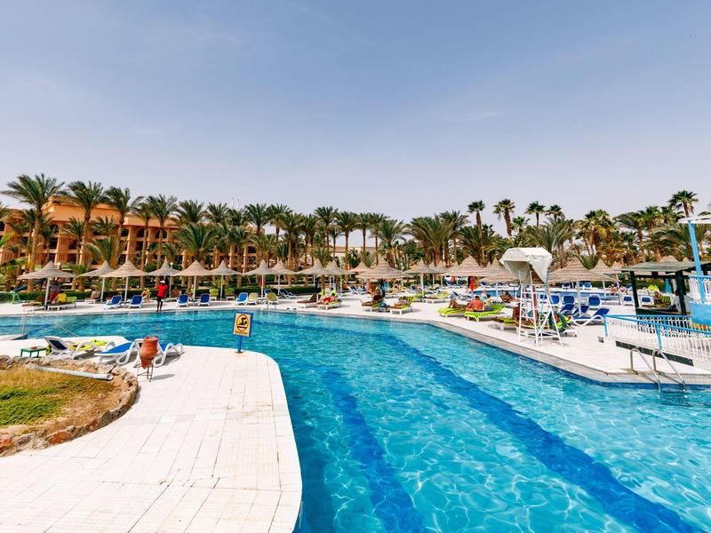 Großer Außenpool mit Liegestühlen und Palmen in einem tropischen Hotelresort.