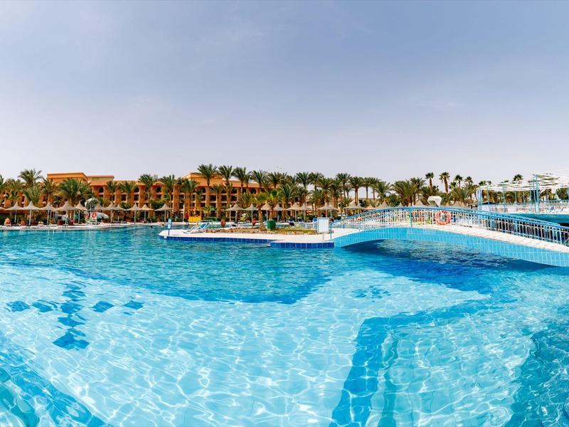 Großer Pool mit klarem blauem Wasser und Brücke im Hotelresort bei sonnigem Himmel.
