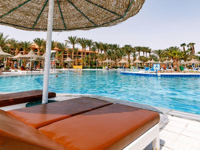 Sonnenliegen und Sonnenschirm am Pool in tropischem Resort bei sonnigem Wetter.