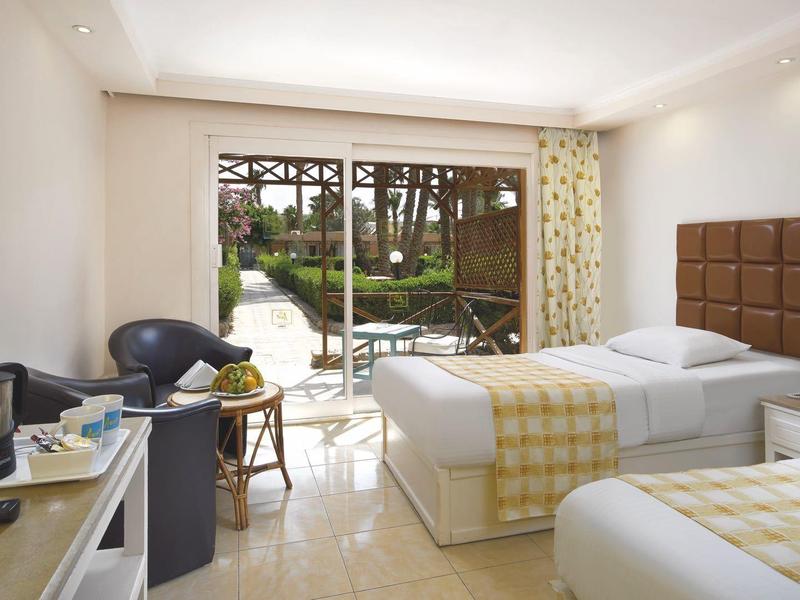 Hell eingerichtetes Hotelzimmer mit zwei Einzelbetten, Stühlen und Blick auf Garten.