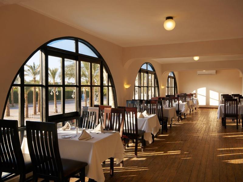 Helles Restaurant mit Holzstühlen, weißen Tischdecken und großen Fensterbögen.