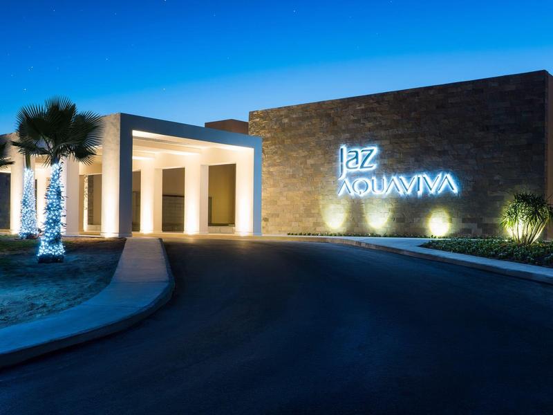 Modernes Gebäude mit beleuchtetem Schriftzug und dekorierten Palmen bei Nacht.