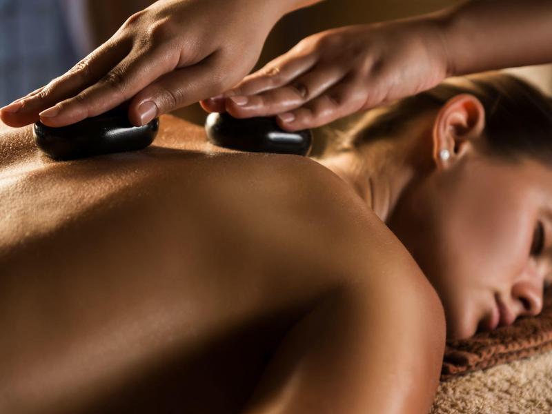 Frau entspannt sich bei Hot-Stone-Massage mit warmen, glatten Steinen auf dem Rücken.