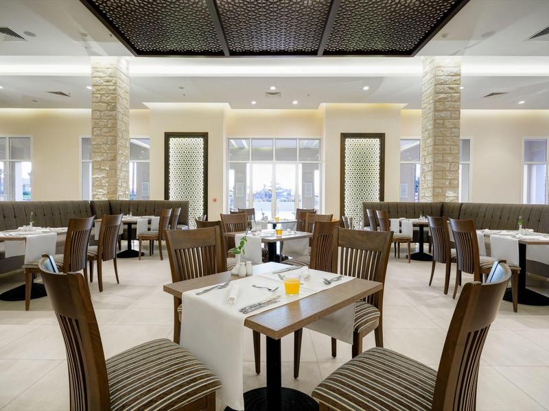 Helles, modernes Restaurant mit weißen Tischen, dunklen Holzstühlen und großen Fenstern.