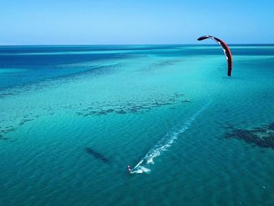 Ein Kitesurfer gleitet auf türkisfarbenem Meer mit klarem Himmel und weitem Horizont.