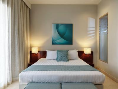 Modern eingerichtetes Hotelzimmer mit großem Bett, zwei Nachttischlampen und abstraktem Bild.