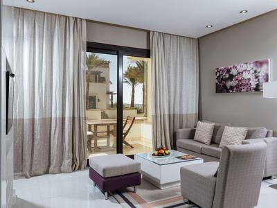 Modern eingerichtetes Wohnzimmer mit Sofa, Stuhl und Blick auf Terrasse und Palmen.