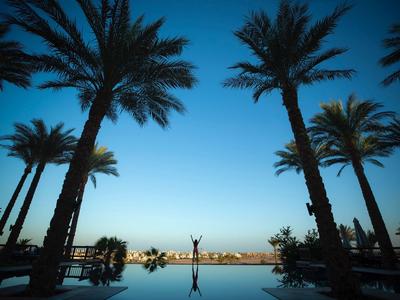 Helle Abendstimmung mit Palmen, einem Pool und einer Person im Hintergrund am Horizont.