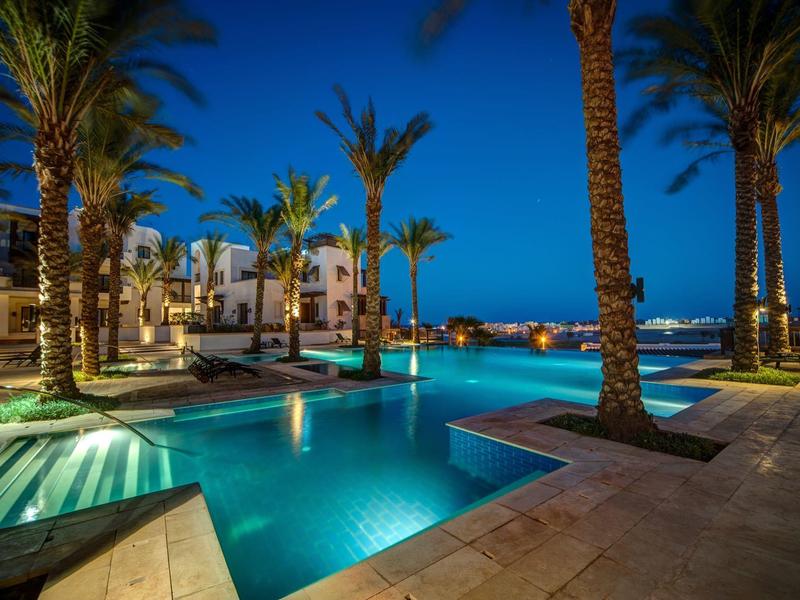 Luxury outdoor pool at night surrounded by palm trees and lounge chairs under a clear sky.