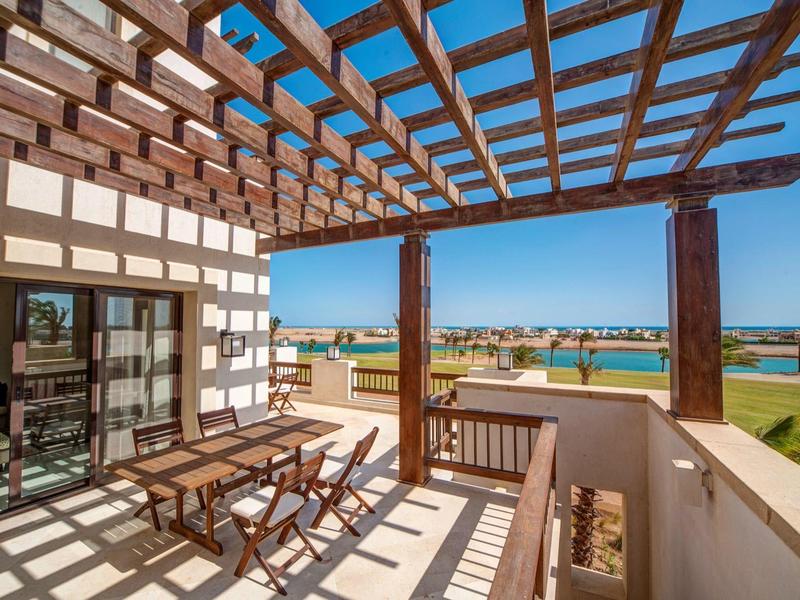 Sunny balcony with wooden pergola and outdoor dining set overlooking green golf course.