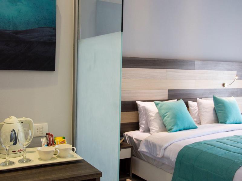 Outdoor terrace with wooden table and chairs, palm trees, and white building under clear blue sky.