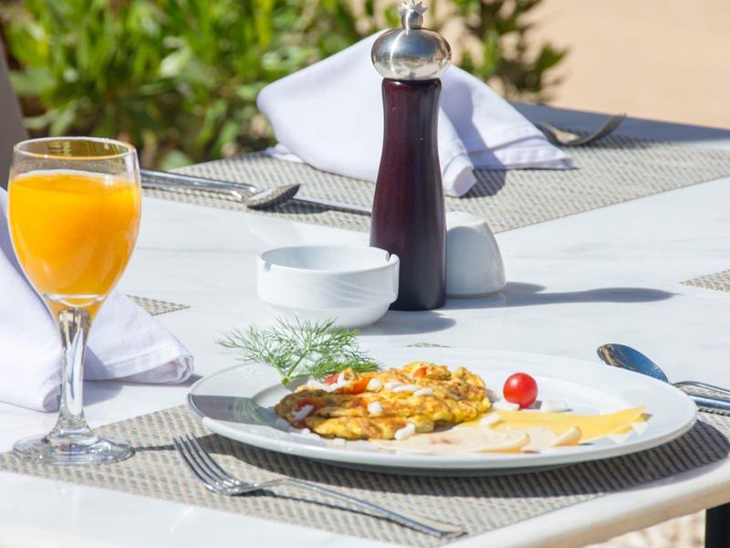 Breakfast plate with scrambled eggs, cherry tomato, juice, and pepper grinder on outdoor table.