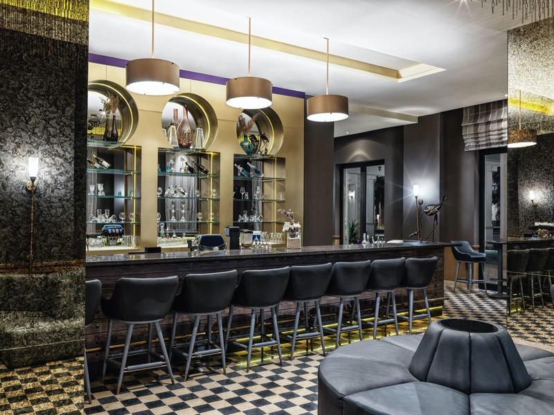 Modern hotel bar with black stools, round mirrors, and elegant lighting fixtures.