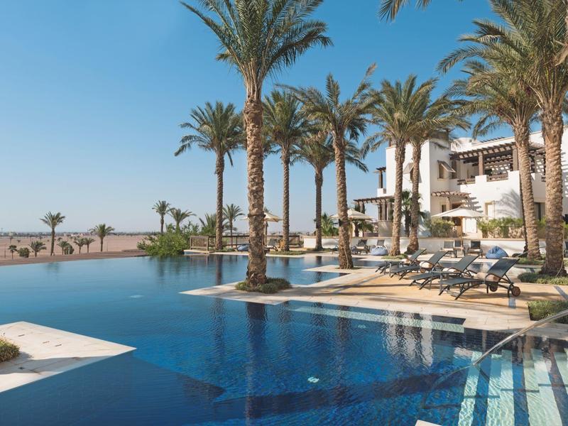 Resort pool with palm trees and lounge chairs under a clear blue sky.