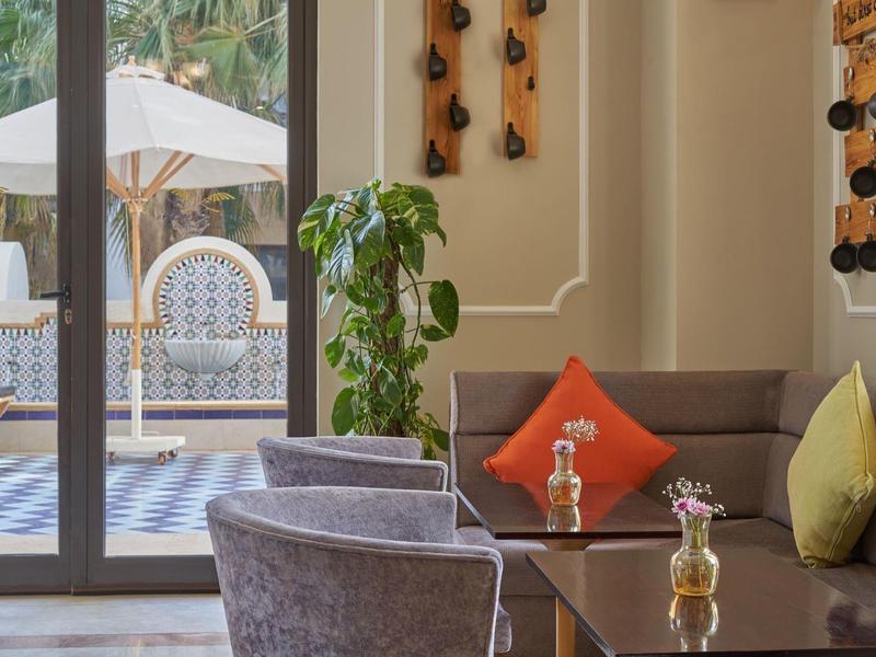 Cozy hotel lounge with plush seating, cushions, plant, and view of outdoor patio with umbrella and bench.