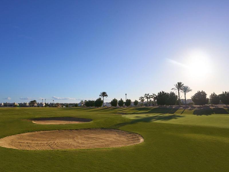 Golf course with sand traps under clear blue sky and bright sun.