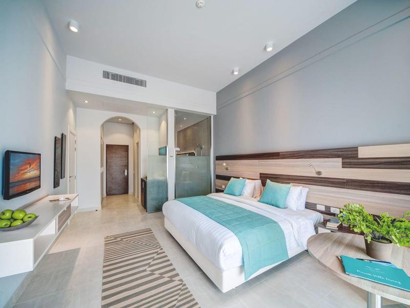 Modern hotel room with a double bed, teal accents, and a glass-partitioned bathroom.