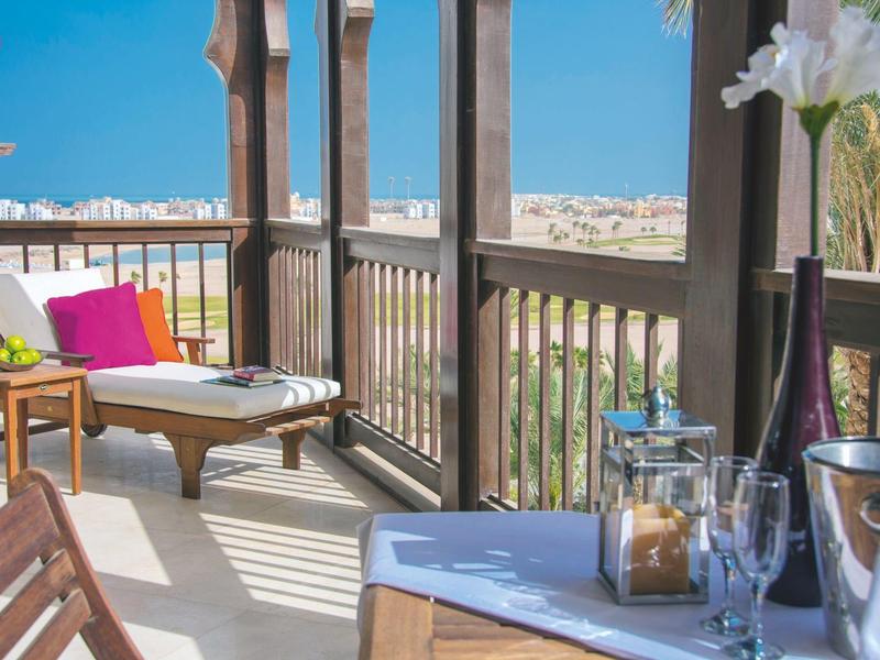 Balcony seating with lounge chair, table, and view of city under clear blue sky.