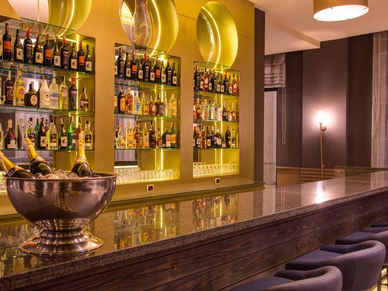 Stylish hotel bar with illuminated shelves of bottles and comfortable stools.