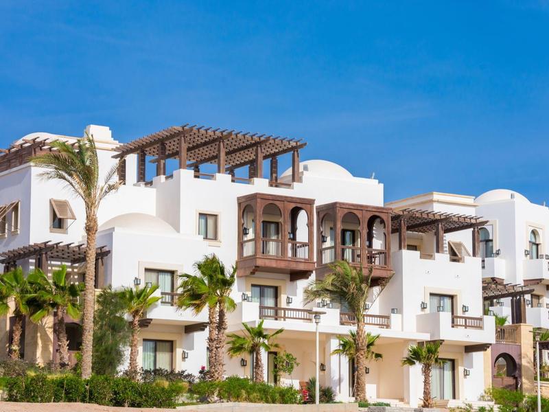 White multi-story hotel with balconies and palm trees under a clear blue sky.