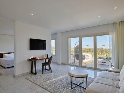 Helles Wohnzimmer mit Sofa, Teppich, Couchtisch, Schreibtisch, Stuhl, TV und großem Panoramafenster.