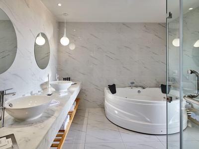 Modernes Badezimmer mit weißer Badewanne, rundem Spiegel, zwei Waschbecken und stilvollen Pendelleuchten.
