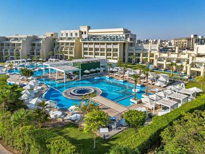 Großer Hotelpool umgeben von Liegestühlen und Sonnenschirmen unter klarem blauem Himmel.