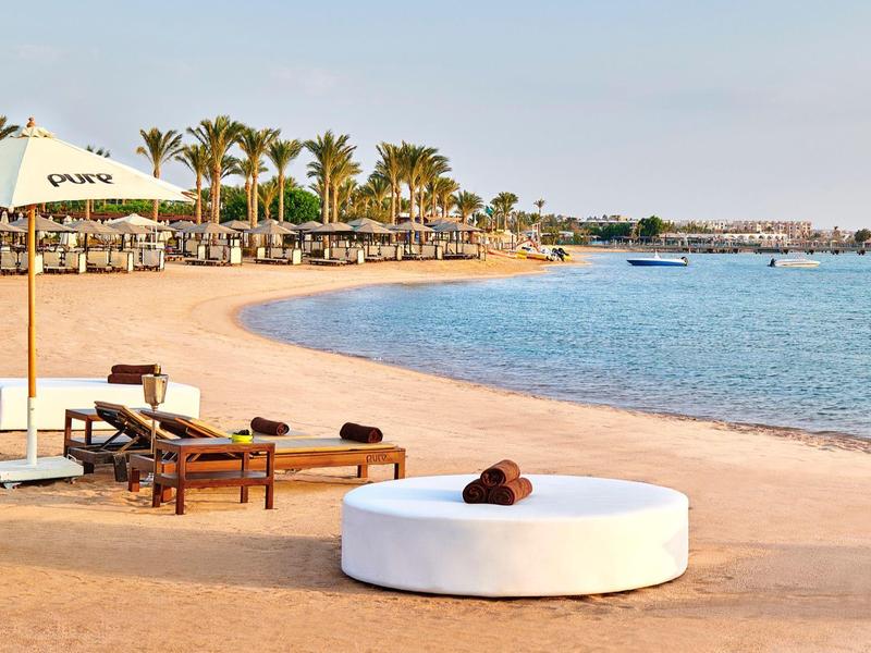 Strand mit Liegestühlen, Sonnenschirmen und Palmen am ruhigen blauen Meer