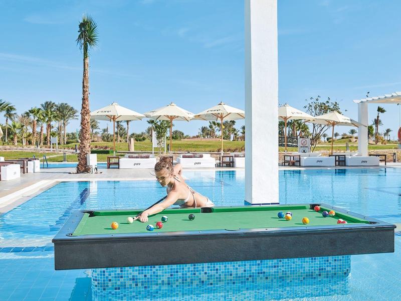 Schwimmender Billardtisch im Pool eines Resorts mit einer Frau, die spielt.