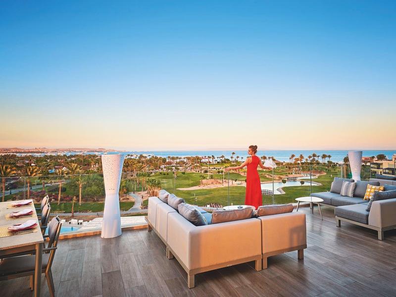 Blick von der Terrasse eines Hotels mit Sitzbereich und einer Frau, die über die Landschaft schaut.