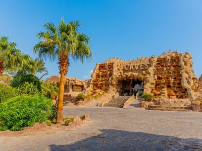 Hotelentree met kunstmatige rotsstructuur en palmbomen onder een heldere blauwe lucht.