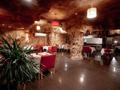 Restaurant in een rotsgrot met rode stoelen en planten.