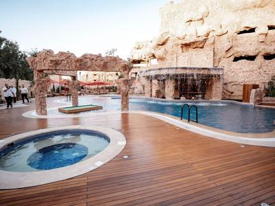 Nowoczesny basen na zewnątrz i jacuzzi z drewnianym tarasem i skalną ścianą w tle.