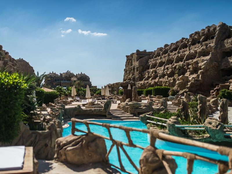 Zwembad met loungegedeelte en rotsgevel onder blauwe lucht in een resort.