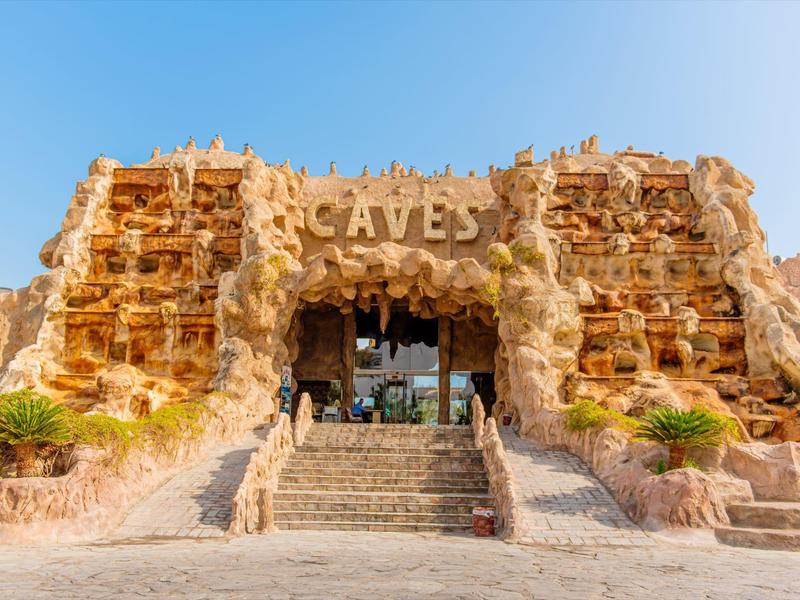 Ingang van een rotsachtig gebouw met het woord CAVES onder een heldere blauwe lucht.
