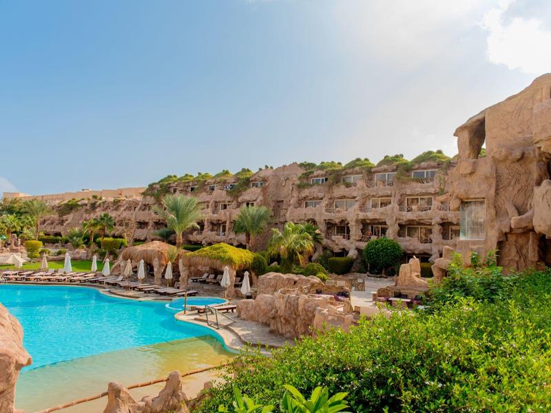 Hotelcomplex met zwembad, rotsformaties en zonnige ligplaatsen onder een heldere hemel.