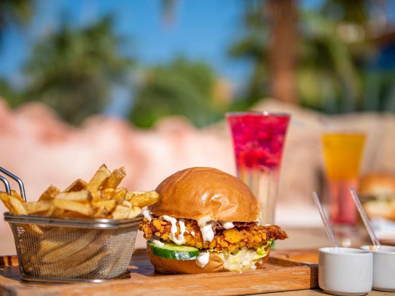 Burger met frietjes en twee kleurrijke drankjes voor een vervaagde palm achtergrond