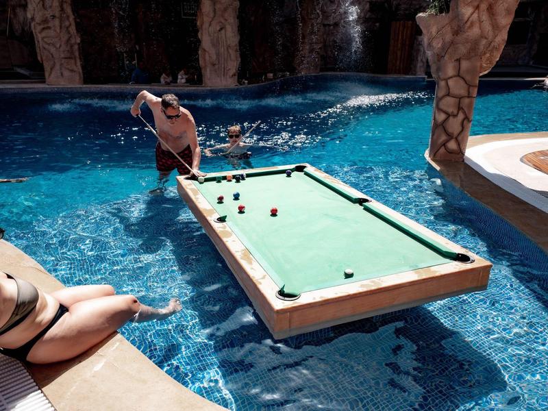 Een zwembad met een ingebouwde pooltafel, twee mensen bij het water, een ontspannen sfeer.