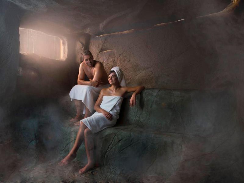 Twee personen ontspannen in een stoomrijke stenen spa-ruimte met gedempt licht.