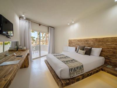 Helles Schlafzimmer mit großem Bett, Holzdetails, TV an der Wand und Zugang zu Balkon mit Glasfront.
