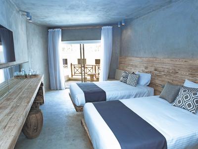 Helles Hotelzimmer mit zwei Doppelbetten, Holzmöbeln und Balkon mit Tisch und Stühlen.